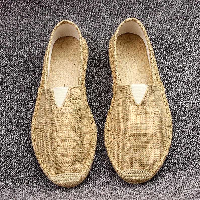 K&ouml;nnte beinhalten: Ein Paar beigefarbene Slipper mit einem Obermaterial aus strukturiertem Webstoff, einer abgerundeten Schuhspitze und einer verst&auml;rkten, mit Jute umwickelten Sohle. Jeder Schuh verf&uuml;gt &uuml;ber einen kleinen wei&szlig;en elastischen Einsatz am Rist.