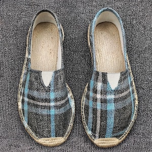 K&ouml;nnte beinhalten: Ein Paar Slipper mit einem schwarz-wei&szlig;-hellblauen Karomuster. Die Schuhe haben eine abgerundete Zehenpartie, einen tief ausgeschnittenen Einstieg mit einem kleinen elastischen Einsatz und eine geflochtene Jute-Borte um die Sohle.