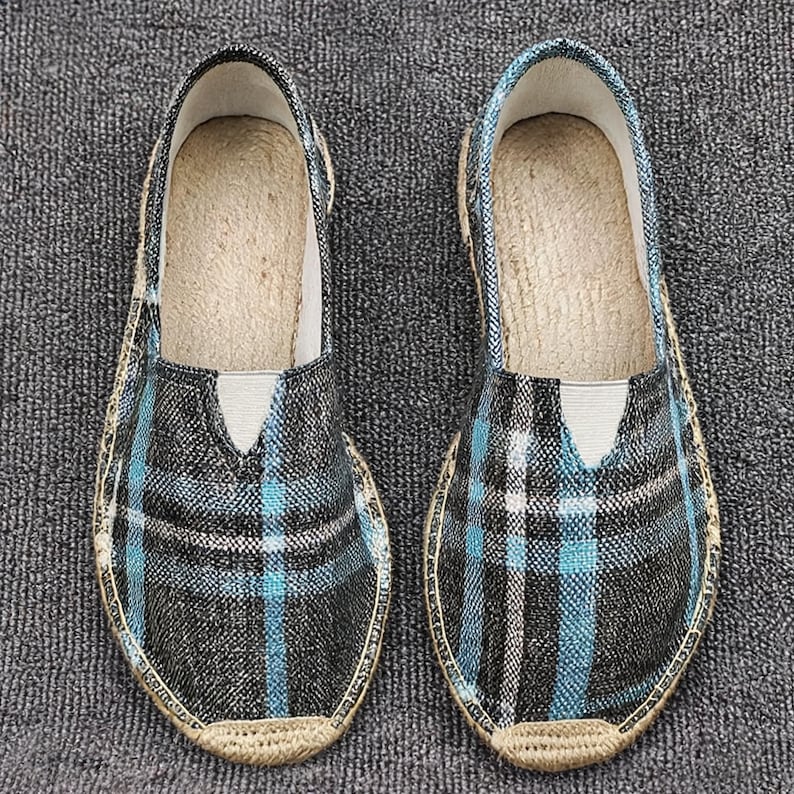 K&ouml;nnte beinhalten: Ein Paar Slipper mit einem schwarz-wei&szlig;-hellblauen Karomuster. Die Schuhe haben eine abgerundete Zehenpartie, einen tief ausgeschnittenen Einstieg mit einem kleinen elastischen Einsatz und eine geflochtene Jute-Borte um die Sohle.