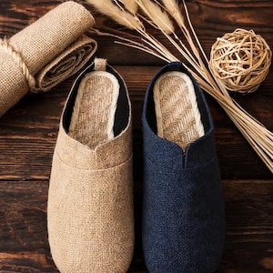 May include: A pair of slip-on shoes featuring a textured fabric upper in beige and navy blue. The interior footbed is lined with a woven straw-like material, and the shoes have a rounded toe design with a low-cut opening for easy entry.