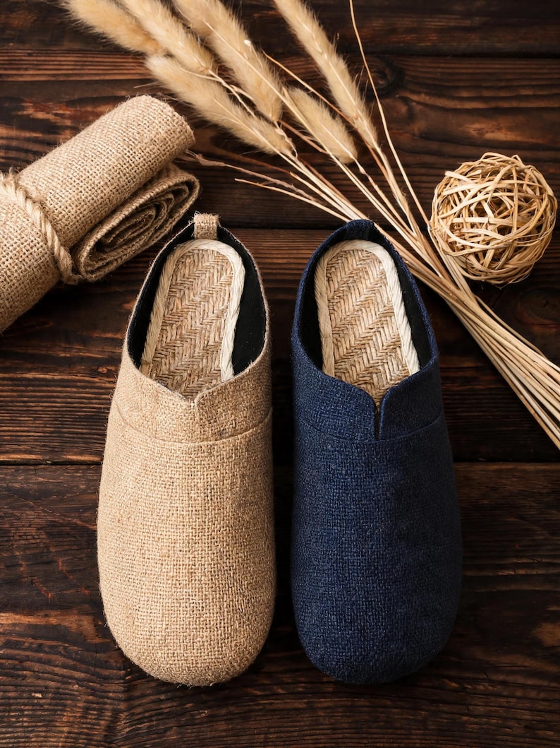 May include: A pair of slip-on shoes featuring a textured fabric upper in beige and navy blue. The interior footbed is lined with a woven straw-like material, and the shoes have a rounded toe design with a low-cut opening for easy entry.