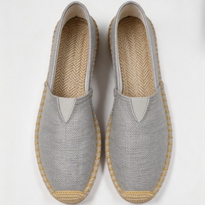 K&ouml;nnte beinhalten: Ein Paar silberne Slipper mit strukturiertem Stoffobermaterial, einem V-f&ouml;rmigen elastischen Einsatz und einer Zwischensohle aus geflochtener Jute mit gelben N&auml;hten am Rand. Das Innere ist mit einer Fischgr&auml;t-Innensohle ausgestattet.