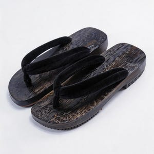 May include: A pair of traditional Japanese geta sandals featuring dark, wood-grain textured platforms and thick, plush black velvet thong straps. The soles are flat with a slightly elevated heel section, showcasing a natural, dark-stained wood finish.