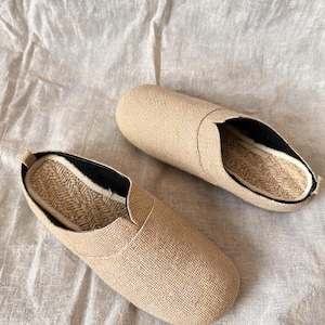 May include: A pair of beige slip-on shoes featuring a textured fabric upper, a rounded toe, and a woven jute insole. The interior lining is black, and the shoes have a low-profile design with a slip-on construction for easy wear and comfort.