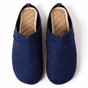 May include: A pair of navy blue slip-on shoes featuring a textured fabric upper and a woven straw-like insole. The shoes have a rounded toe, a low-cut collar, and a small pull tab at the heel, providing a simple and functional footwear design.