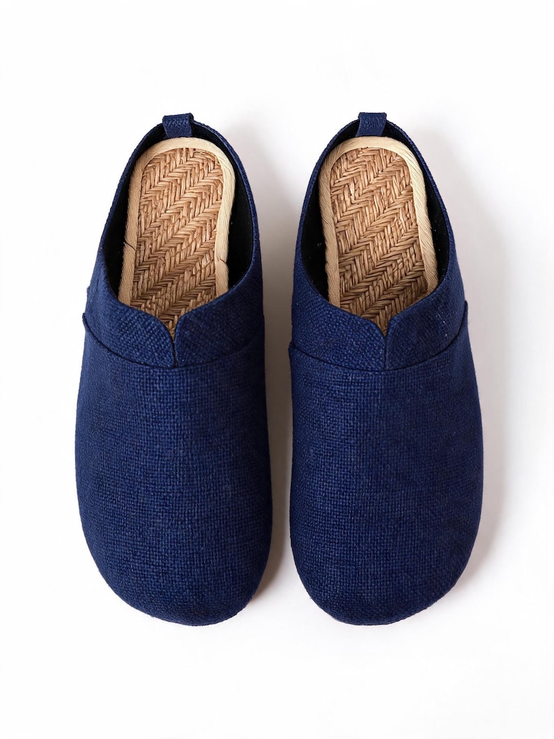 May include: A pair of navy blue slip-on shoes featuring a textured fabric upper and a woven straw-like insole. The shoes have a rounded toe, a low-cut collar, and a small pull tab at the heel, providing a simple and functional footwear design.