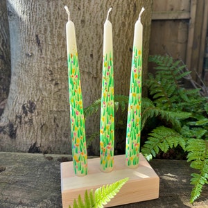 May include: Three tall white candles with a green and floral design. The candles are on a wooden stand.