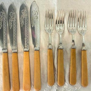May include: A set of antique silverware including six knives and four forks. The knives have ornate silver blades and light brown handles. The forks have silver tines and light brown handles. The silverware is arranged on a white surface.