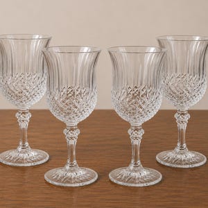May include: A set of four clear crystal wine glasses featuring a flared rim, a vertical ribbed upper bowl, and a diamond-cut pattern on the lower bowl. Each glass has a faceted stem and a circular base with a starburst design on the underside.