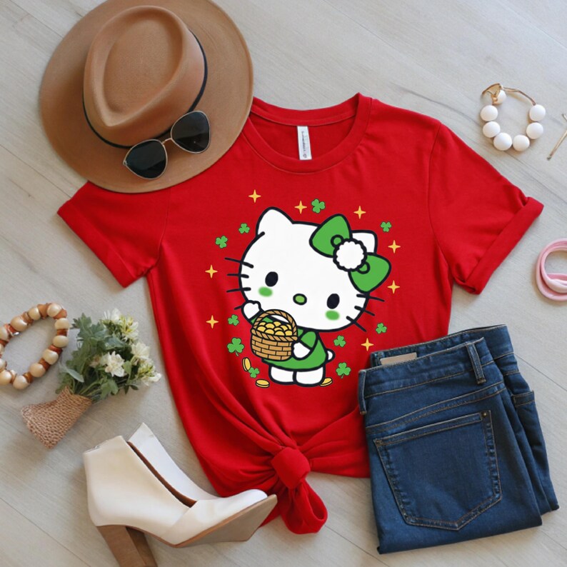 May include: A red t-shirt featuring a cartoon cat character with a green bow, holding a basket of gold coins, surrounded by shamrocks. The shirt is styled with blue jeans, white boots, and a brown hat.