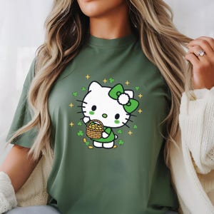 May include: Green t-shirt featuring a cartoon character with a white head, green bow, and green outfit, holding a basket of gold coins. The design includes shamrocks and gold stars, celebrating St. Patrick's Day.