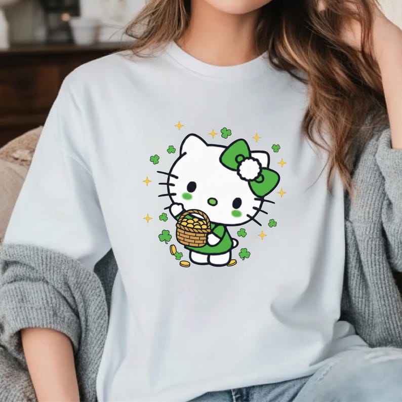 May include: White t-shirt featuring a cartoon character with a green bow, dress, and a basket of gold coins. The design includes green clovers and yellow stars, creating a festive St. Patrick's Day theme.