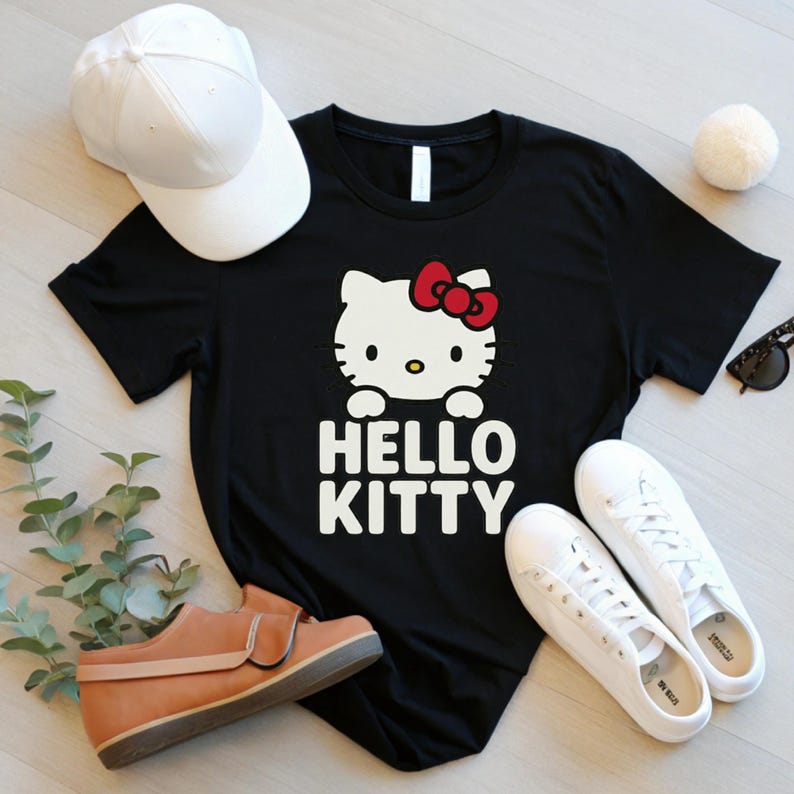 Peut inclure: T-shirt noir avec un motif Hello Kitty, un n&oelig;ud rouge et le texte "HELLO KITTY" en blanc. L'image pr&eacute;sente &eacute;galement une casquette de baseball blanche, des baskets blanches et des chaussures marron.