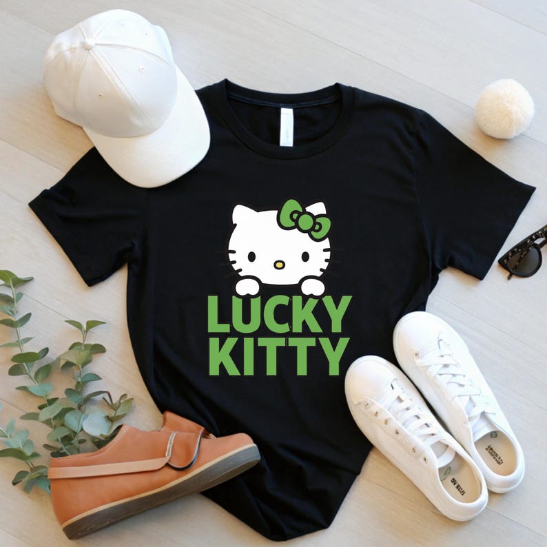 Peut inclure: T-shirt noir avec un motif Hello Kitty blanc, un n&oelig;ud vert et le texte "LUCKY KITTY" en vert. L'image comprend &eacute;galement une casquette de baseball blanche, des baskets blanches, des lunettes de soleil et une chaussure marron.