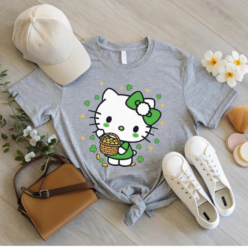 May include: A gray t-shirt featuring a cartoon character with a green bow, holding a basket of gold coins. The design includes green shamrocks and gold stars. A beige baseball cap and white sneakers are also visible.