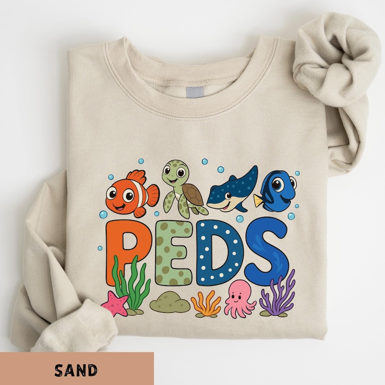 A beige t-shirt with a colorful graphic design featuring cartoon fish and sea creatures, along with the word "PEDS" written in a playful font.