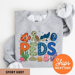 A gray sweatshirt with a colorful graphic design featuring cartoon sea animals and the word "PEDS" printed on it.