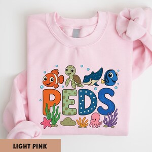 A pink sweatshirt with a colorful graphic design featuring cartoon sea animals such as Nemo, Dory, and Patrick.
