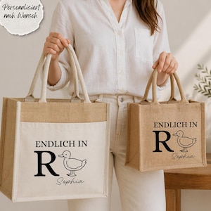 Könnte beinhalten: Zwei Tragetaschen aus beigem und weißem Stoff. Die Taschen haben Griffe und eine Vordertasche. Auf der Vorderseite ist der Text "ENDLICH IN R" mit einer Entenillustration und dem Namen "Sophia" aufgedruckt.