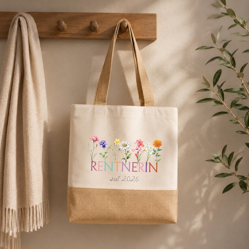 May include: A beige canvas tote bag with a brown burlap base. The front features a colorful floral illustration above the text RENTNERIN and the year 2026. The bag has two long shoulder straps and a rectangular shape with a clean, simple design.