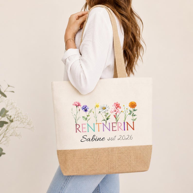 May include: A cream-colored canvas tote bag with a brown burlap base. The bag features a colorful floral illustration above the text "RENTNERIN" in multi-colored letters, followed by the black script text "Sabine seit 2026" printed on the front.