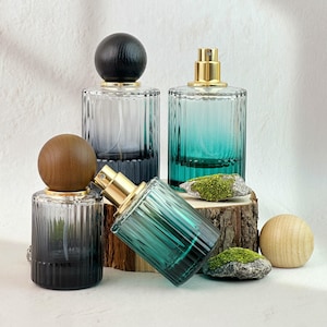 May include: Several glass perfume bottles with ribbed sides and gold-colored sprayers. The bottles are in shades of blue and green, with wooden and black spherical stoppers. Some bottles are upright, while others are on their side.