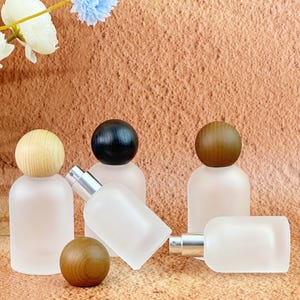 May include: A collection of frosted glass perfume bottles with wooden and black spherical caps. The bottles have silver spray nozzles. One bottle is lying on its side. The background is a textured, light brown surface.