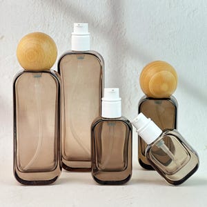 May include: A collection of brown glass bottles with white pump tops and wooden sphere caps. The bottles vary in size and shape, suitable for storing liquids. The design is minimalist and elegant.