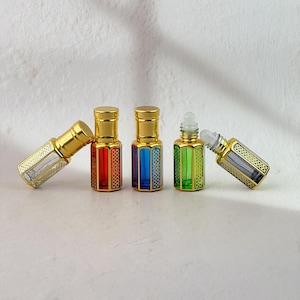 May include: A collection of five small glass perfume bottles with gold-colored metal caps and decorative gold lattice overlays. The bottles feature various transparent colors including red, blue, and green, with some shown upright and others lying on their sides.