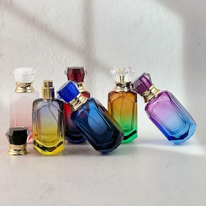 May include: An assortment of perfume bottles in various colors, including pink, yellow, blue, and purple. The bottles have gold accents and crystal-like stoppers. The bottles are arranged on a white surface.