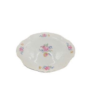Könnte beinhalten: Eine weiße, ovale Servierplatte mit gewelltem Rand. Die Platte ist mit floralen Mustern in Rosa, Blau und Gelb verziert. Die Blumen sind in Clustern über die Oberfläche angeordnet und verleihen Eleganz.