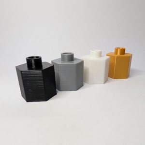 Pode incluir: Quatro rolhas de garrafa hexagonais em fila. As rolhas são pretas, cinzentas, brancas e douradas. Cada rolha tem um topo cilíndrico. As rolhas são feitas de um material sólido e têm uma superfície texturizada.