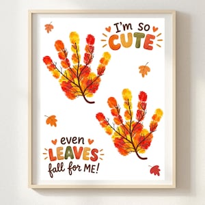 Op de afbeelding: Een ingelijste print met twee handafdruk-vormige bomen met herfstkleurige bladeren in rood, oranje en geel. De tekst luidt I'm so CUTE en even LEAVES fall for ME!, omringd door kleine oranje en rode bladillustraties op een witte achtergrond.