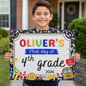 Op de afbeelding: Een rechthoekig bord met een zwart-witte rand in een notitieboekpatroon. De tekst luidt OLIVER'S first day of 4th grade 2026. De afbeeldingen bevatten kleurrijke kleurpotloden, een gele schoolbus, een rode appel en een smiley-icoon.