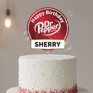 May include: A white cake with red sprinkles at the base, topped with a Dr. Pepper-themed cake topper. The topper is a red circle with "Happy Birthday" and the Dr. Pepper logo, and a banner that says "SHERRY".