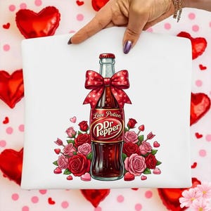 May include: White graphic featuring a Dr. Pepper bottle labeled "Love Potion" with a red bow, surrounded by roses and hearts. The bottle is a dark brown color.