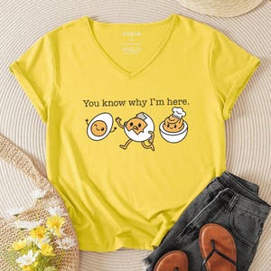 May include: Yellow V-neck t-shirt with the text "You know why I'm here." and a cartoon egg design. The design features three eggs: one whole, one running out of its shell, and one in a bowl with a chef's hat.
