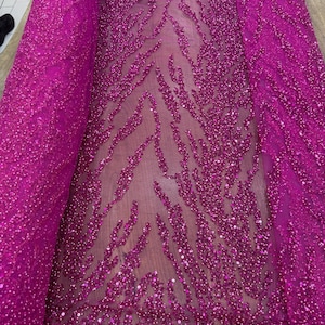 May include: A bolt of vibrant fuchsia fabric featuring a sheer mesh base adorned with an intricate, dense pattern of matching sequins. The sequins are arranged in organic, flowing, wave-like shapes that create a textured, shimmering surface.