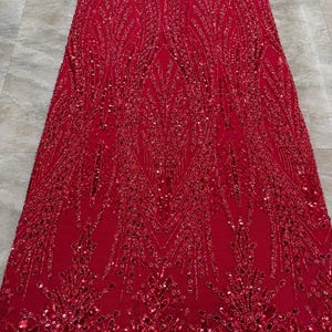 May include: A vibrant red fabric featuring an intricate, symmetrical pattern of embroidered leaves and stems. The design is heavily embellished with matching red sequins and beads that create a textured, shimmering surface across the entire textile.