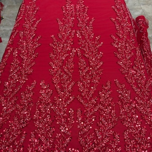 May include: A rich red fabric with elaborate floral embroidery. The design showcases detailed, sequined branches and leaves, giving a textured and luxurious look. Suitable for special occasion wear or decorative projects.