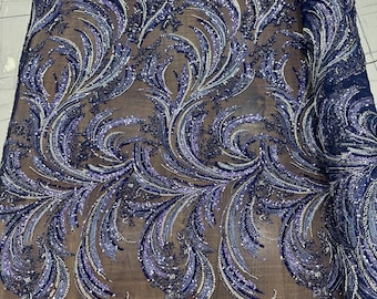 May include: Navy blue fabric with an intricate floral design. The design features swirling patterns in shades of blue, silver, and purple, embellished with sequins. The fabric is partially rolled, showcasing the detailed embroidery.
