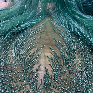 Può includere: Tessuto verde smeraldo con perline, con una delicata trama a rete. Il tessuto è adornato con piccole perline rotonde e paillettes, creando un effetto scintillante. Il design presenta intricati motivi di abbellimenti con perline.