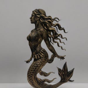 May include: A bronze mermaid sculpture with flowing hair and a detailed fishtail. The mermaid is in profile, with arms outstretched. The sculpture has a textured surface and is set against a plain background.