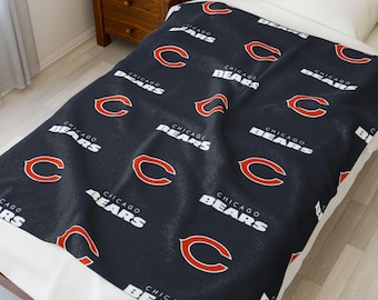 May include: A navy blue blanket featuring the Chicago Bears logo and team name in white and orange. The repeating pattern includes the letter "C" and the words "Chicago Bears". The blanket is on a white bed.