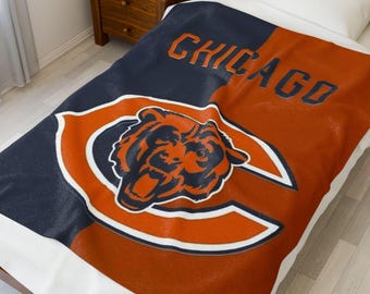 Peut inclure: Une couverture Chicago Bears bleu marine et orange. La couverture présente le logo de l'équipe, une tête d'ours à l'intérieur d'un C orange bordé de blanc, et le mot "CHICAGO" en lettres orange. La couverture est sur un lit avec un oreiller blanc.