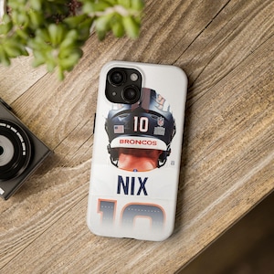Puede incluir: Funda blanca para iPhone con diseño de casco de fútbol. Muestra el número 10 y el nombre NIX. El casco es negro y azul marino, con la palabra "BRONCOS" debajo. Sobre una superficie de madera.