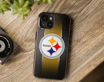 May include: Black smartphone case with a yellow stripe and the Pittsburgh Steelers logo. The logo features a white circle with the word "Steelers" and three stars in yellow, red, and blue. The case is on a wooden surface.