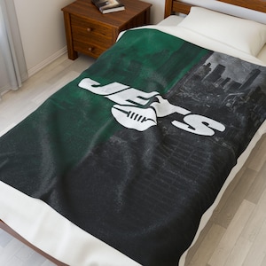 Puede incluir: Una manta verde, negra y blanca con el logotipo de los New York Jets y la palabra "JETS" en blanco. La manta tiene un diseño de paisaje urbano en el lado derecho. La manta está sobre una cama con una almohada blanca.