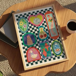 May include: A framed artwork featuring colorful, whimsical illustrations on a checkered background. The artwork includes images of a cake, cherries, a duck, and other decorative elements. A cup of coffee and books are on a wooden table.