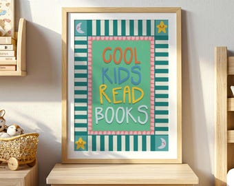 May include: A framed print with the words "COOL KIDS READ BOOKS" in colourful letters. The artwork has a green background with a pink border and a striped teal and white frame. The print is displayed on a wooden bedside table next to a bed.
